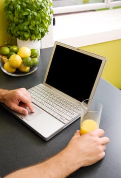A computer in the kitchen with a male hand using the touch pad.  The laptop has a completely black screen for easy editing.