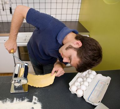 A happy male in the kitchen making pasta by hand 