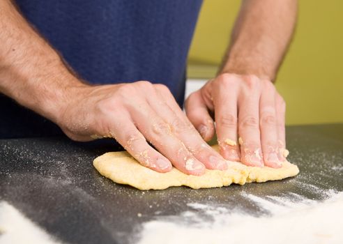 A detail image of a male making fresh pasta on the counter.  The pasta dough is being flatened before rolling through the pasta machine