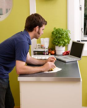 A young cook at home in an apartment kitche, looking on the computer at a recipe while making fresh pasta.