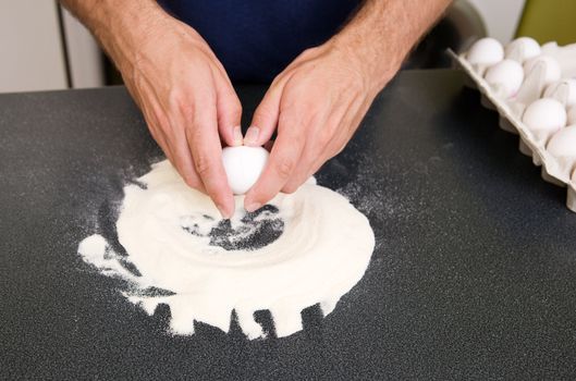 A young man making pasta at home in an apartment kitchen - Cracking an egg into the flour to be mixed by hand on the counter