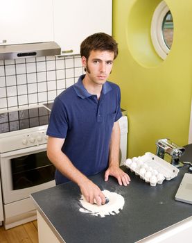 A young man making pasta at home in an apartment kitchen.