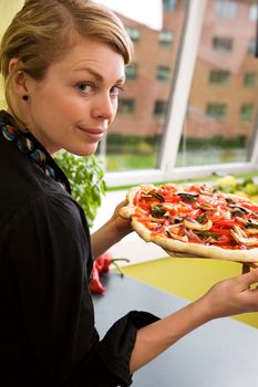 A young woman presents a homemade italian style pizza fresh from the oven in her apartment kitchen.