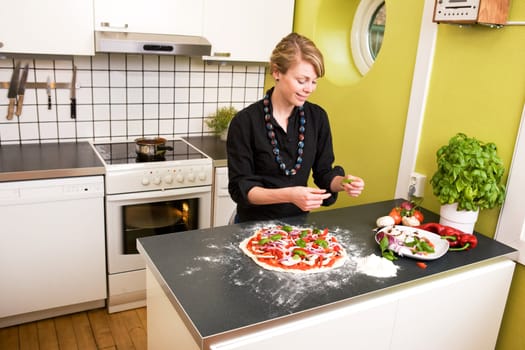 A young female in an apartment kitchen making an itialian style pizza.