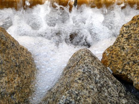 A abstract photograph of some frothy water hitting stones.