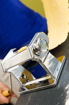 A young female stretching out pasta over the counter from a manual pasta machine at home in the kitchen.