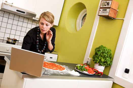 A young female cooking the the kitchen following a recipe on the computer.