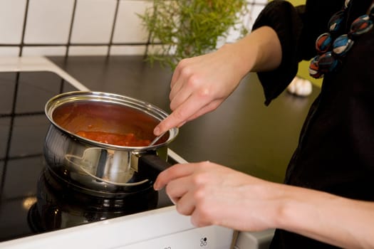 A female making pizza sauce on the stove top in her kitchen.