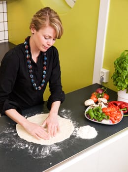 A young woman is making pizza dough on the kitchen counter at home in her apartment - viewed from above.
