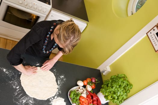 A young woman is making pizza dough on the kitchen counter at home in her apartment - viewed from above.