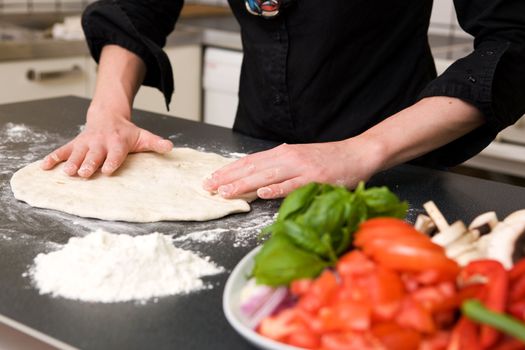 A detail image of a woman making pizza dough on the kitchen counter.  Shallow depth of field is used with the focus on the hands and dough.