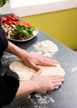 A detail image of a woman making pizza dough on the kitchen counter.