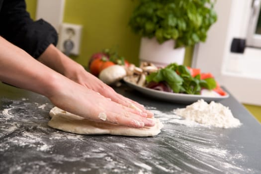 A pair of female hands prepare some bread dough on the counter for pizza.