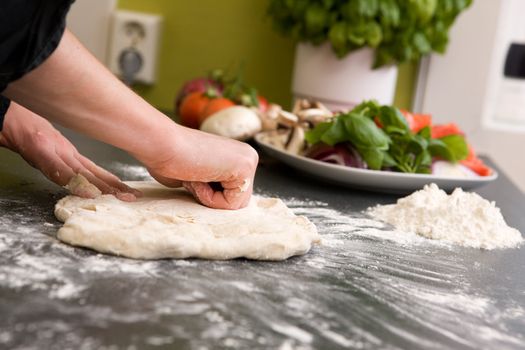 A pair of female hands are kneading bread dough into a pizza form.