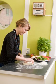 A young woman is making pizza dough on the kitchen counter at home in her apartment.