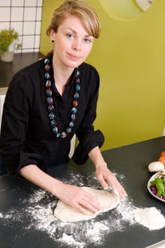 A young woman is making pizza dough on the kitchen counter at home in her apartment.