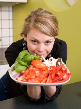 A female holding a plate of vegetables out to the viewer.  Shallow depth of field is used - with focus on the models face and eyes.