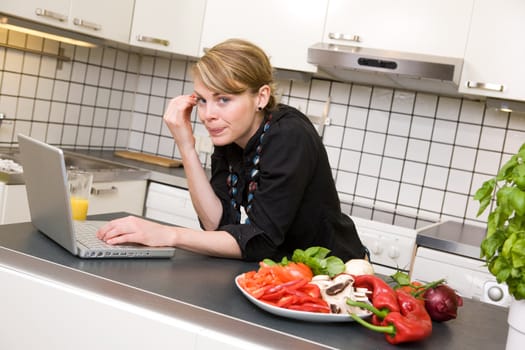 A young female woman using the computer in the kitchen over a small healthy lunch.