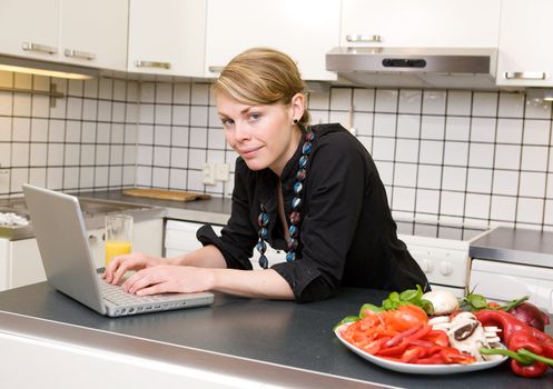 A young female eats a healthy lunch of vegetables at the kitchen counter while using the computer.