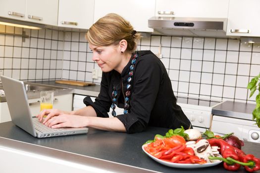 A young female eats a healthy lunch of vegetables at the kitchen counter while using the computer.