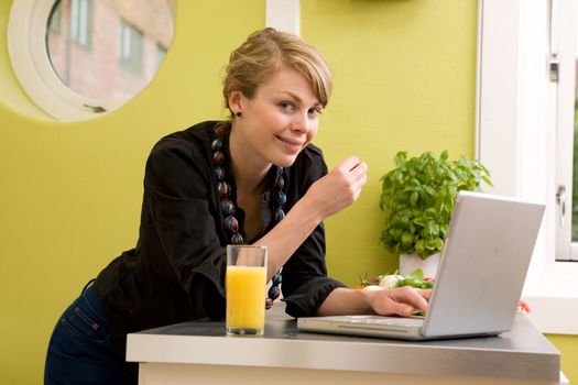A female smiles at the camera while eating halthy lunch and using the computer