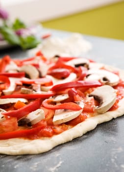 A homemade pizza sitting on the counter ready to be put in the oven. - Shallow depth of field is used to isolate the pizza.