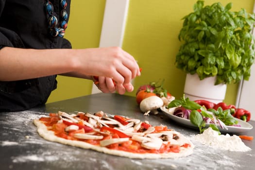 A young female making an italian style pizza at home in her apartment kitchen. - Shallow depth of field is used, with focus on the pizza and hands.