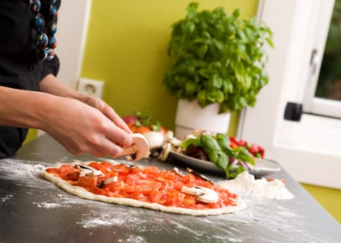 A young female making an italian style pizza at home in her apartment kitchen. - Shallow depth of field is used, with focus on the pizza and hands.