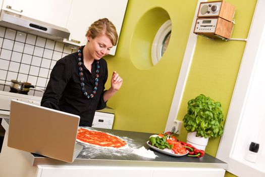 A young female cooking the the kitchen following a recipe on the computer.