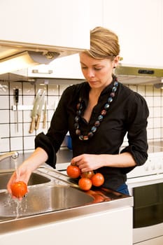 A woman is washing fresh tomatoes from the vine in the sink at home in the kitchen.