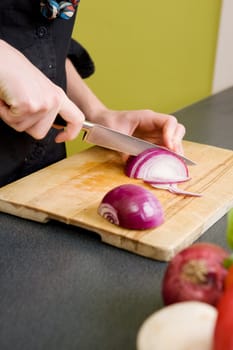 A detail image of a woman cutting a red onion at home in the kitchen.