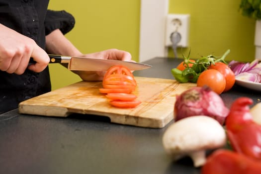 A detail image of a woman slicing tomatoes on a cutting board at home. - shallow depth of field with the focus on the tomato and knife