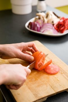 A detail image of a woman slicing tomatoes on a cutting board at home. - shallow depth of field with the focus on the tomato and knife