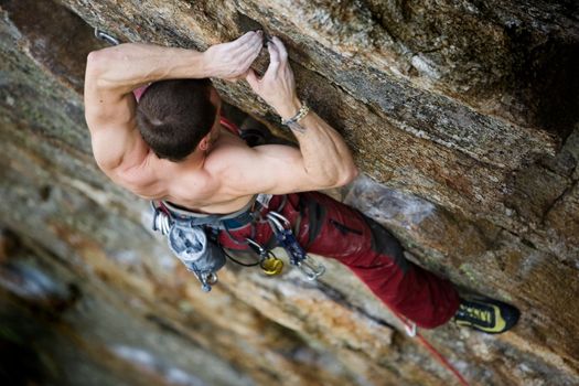 A male climber, viewed from above, climbs a very high and steep crag.