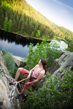 A female climber on a steep rock face viewed from above with the belayer in the background.  The climber has proudly reached the top. Shallow depth of field is used to isolated the climber.