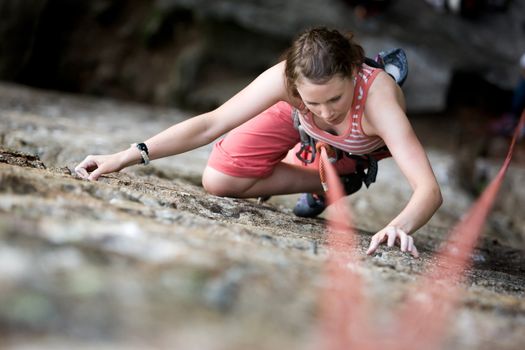 A female climber on a steep rock face viewed from above with the belayer in the background.  Shallow depth of field is used to isolated the climber.