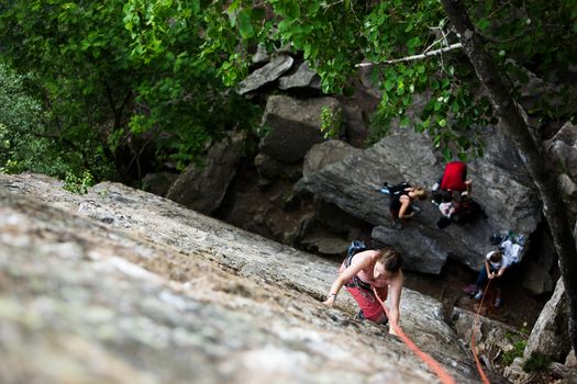 A female climber on a steep rock face viewed from above with the belayer in the background.  Shallow depth of field is used to isolated the climber.