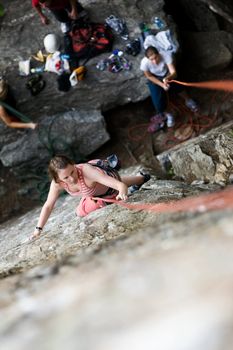 A female climber on a steep rock face viewed from above with the belayer in the background.  Shallow depth of field is used to isolated the climber.