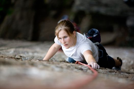 A female climber on a steep rock face looking for the next hold.  Shallow depth of field is used to isolate the climber.