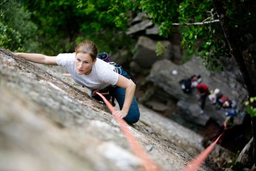 A female climber on a steep rock face.  Shallow depth of field is used to isolated the climber.  Focus is on the head, shoulders and arms of the climber.