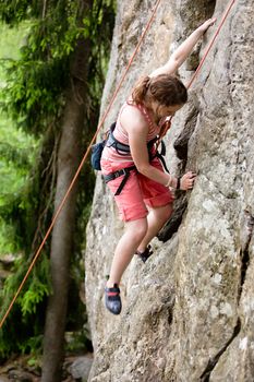 A female climber, climbing using a top rope on a steep rock face (crag).  A shallow depth of field has been used to isolated the climber, with the focus on the head and right hand.