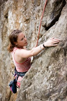 A female climber, climbing using a top rope on a steep rock face (crag).  A shallow depth of field has been used to isolated the climber, with the focus on the head and eyes.