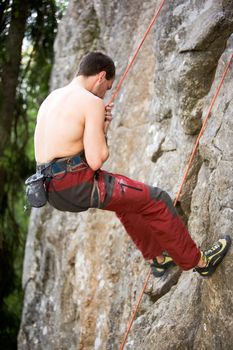 A male climber repells down a rock face - crag.