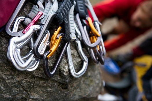 A pile of quick draw carabiners with climbers out of focus in the background.