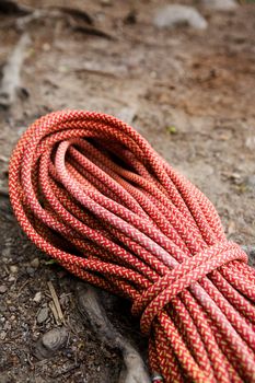 A climbing long orange climbing rope coiled up and placed on the ground.  The image has shallow depth of field.