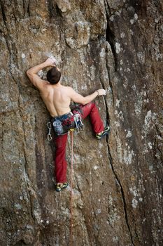 A male climber against a large rock face climbing lead against a magnificant landscape.