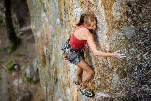 An eager female climber on a steep rock face looks for the next hold - viewed from above.  Shallow depth of field is used to isolated the climber with the focus on the head.