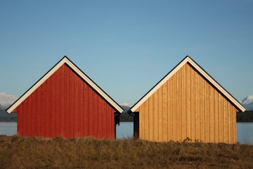 Two small almost identical houses by the sea, one yellow and one red.