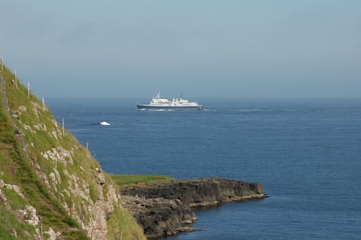 Ferry boat passing steep volcanic cliffs in Suduroy, Faroe Islands. 