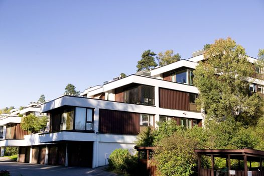 A functional style terrace apartment building against a blue sky and lots of greenery